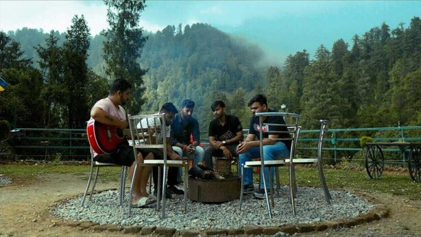 A group of people sitting around a metal table outdoors with a forested hill in the background.