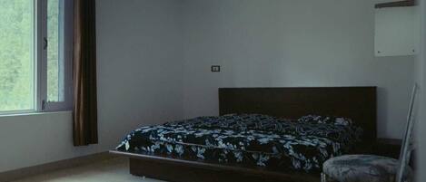 A bedroom with a bed, a chair, a window with curtains, and a wall-mounted light fixture.