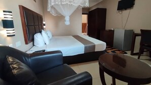 Habitación de hotel con cama, sofá de cuero negro, una mesita, ventilador de techo y televisión montada en la pared.