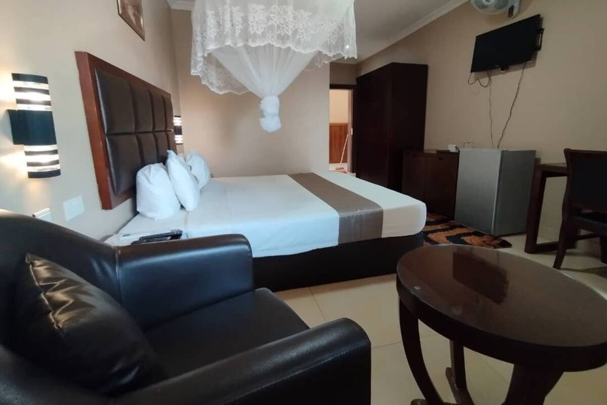 A hotel room with a bed, a black leather sofa, a small table, a ceiling fan, and a TV mounted on the wall.