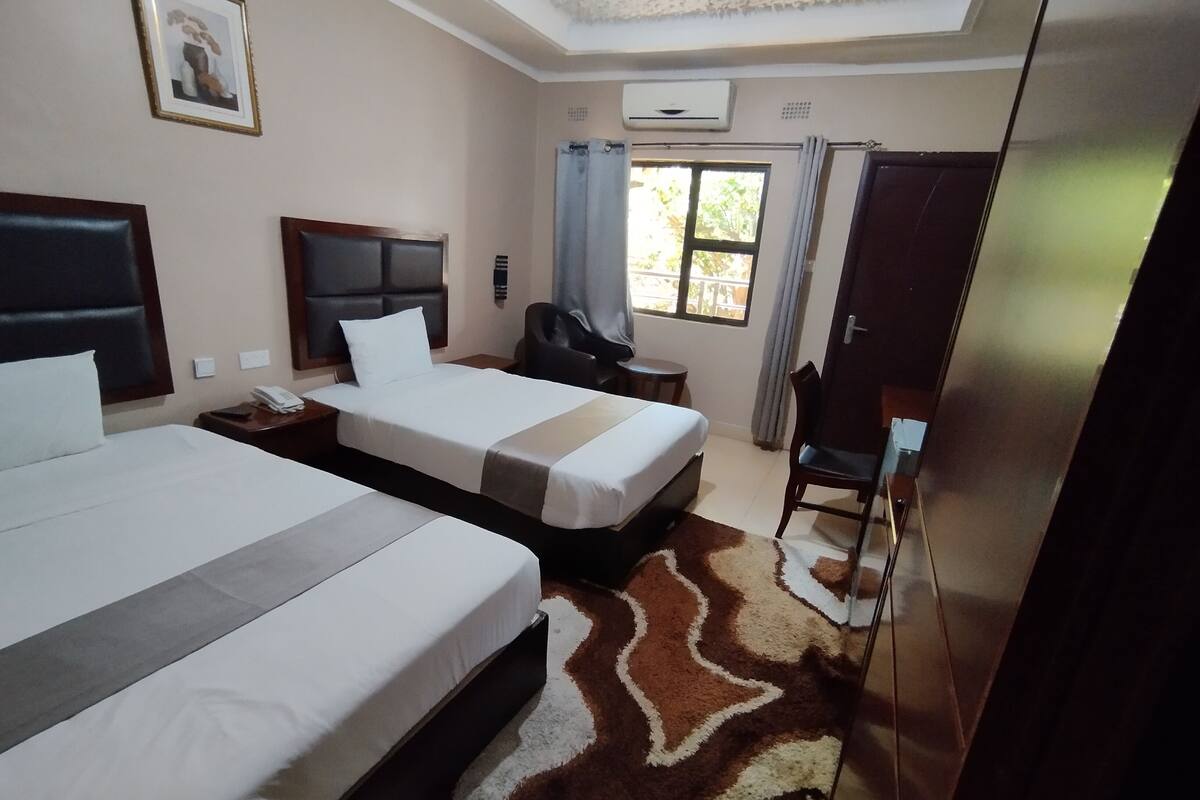 A hotel room with two beds, a desk, a chair, a wardrobe, and a window with curtains.