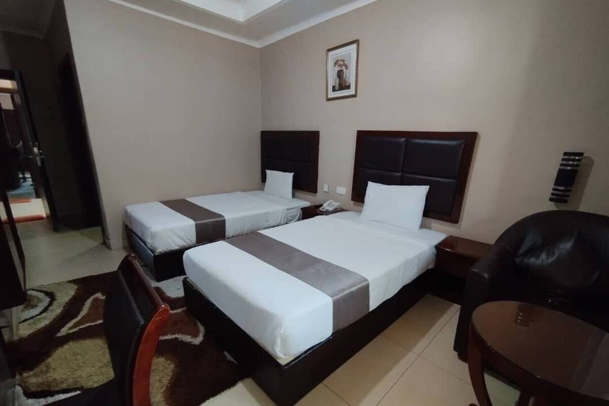 A hotel room with two single beds, a desk, a chair, and a small table.