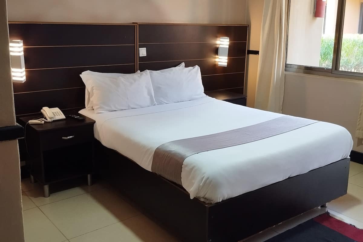 A hotel room with a large bed, bedside lamps, a telephone, and a window with curtains.
