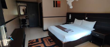 A hotel room with a bed, bedside table, nightstand, wardrobe, and a ceiling fan.