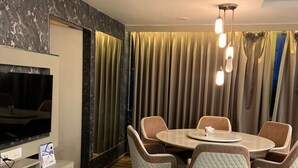 A modern dining area with a round table and six chairs, a flat-screen TV on a white cabinet, and a ceiling light fixture. - Hotel BTP INN (Nagpur)