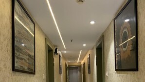 A hallway with framed artwork on the walls, a marble floor, and recessed lighting. - Hotel BTP INN (Nagpur)