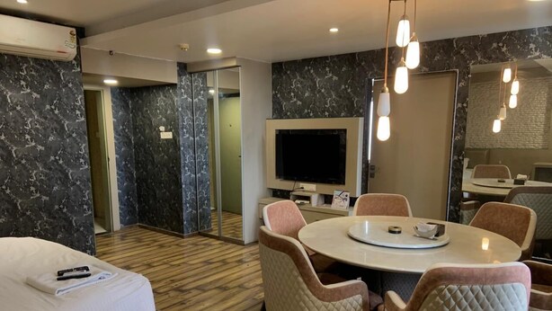 A hotel room with a bed, a round dining table with chairs, a flat-screen TV, and a minibar. - Hotel BTP INN (Nagpur)