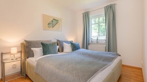 A neatly arranged bedroom with a bed, bedside table, and a window with curtains.