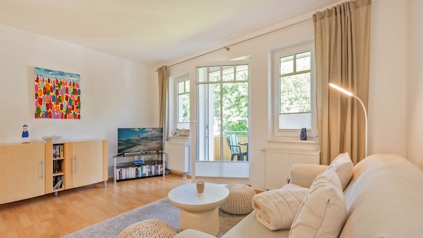 A modern living room with a sofa, coffee table, and a television. There is a bookshelf and a painting on the wall.