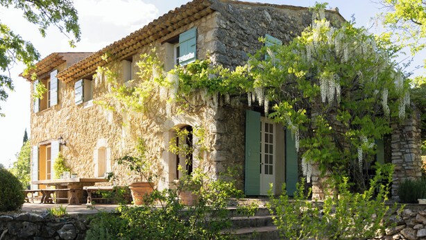 Un bâtiment en pierre avec un toit en tuiles, un banc en bois et des plantes en pot.