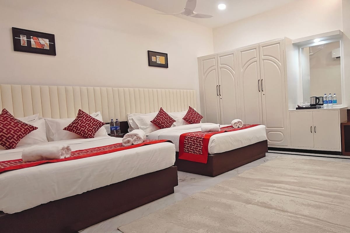 A hotel room with two beds, a wardrobe, a mirror, and a small desk with water bottles.