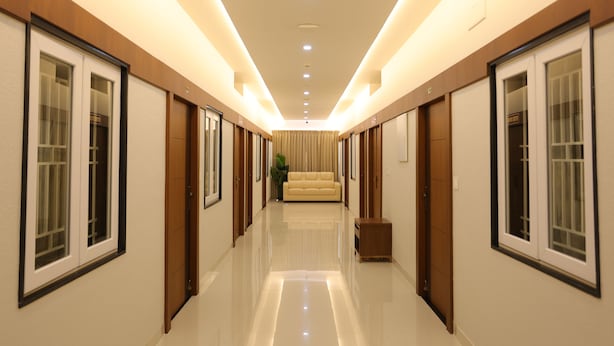 A modern hotel hallway with a polished floor, wooden paneling, and a central seating area. - Aswin Residency (Namakkal)