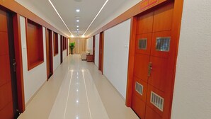 A hotel corridor with wooden doors, a tiled floor, and a ceiling with recessed lighting. - Aswin Residency (Namakkal)