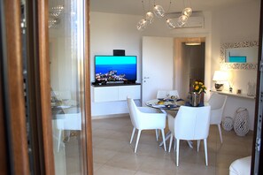 A dining area with a television mounted on the wall, a dining table with chairs, and a decorative lamp on a side table. - Mediterranean Apartment (Taormina)