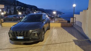 A black SUV parked in a covered parking area with a view of a coastal town and hills in the background. - Mediterranean Apartment (Taormina)