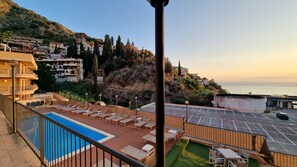 A rooftop pool area with lounge chairs, a swimming pool, and a view of the sea and hillside buildings. - Mediterranean Apartment (Taormina)