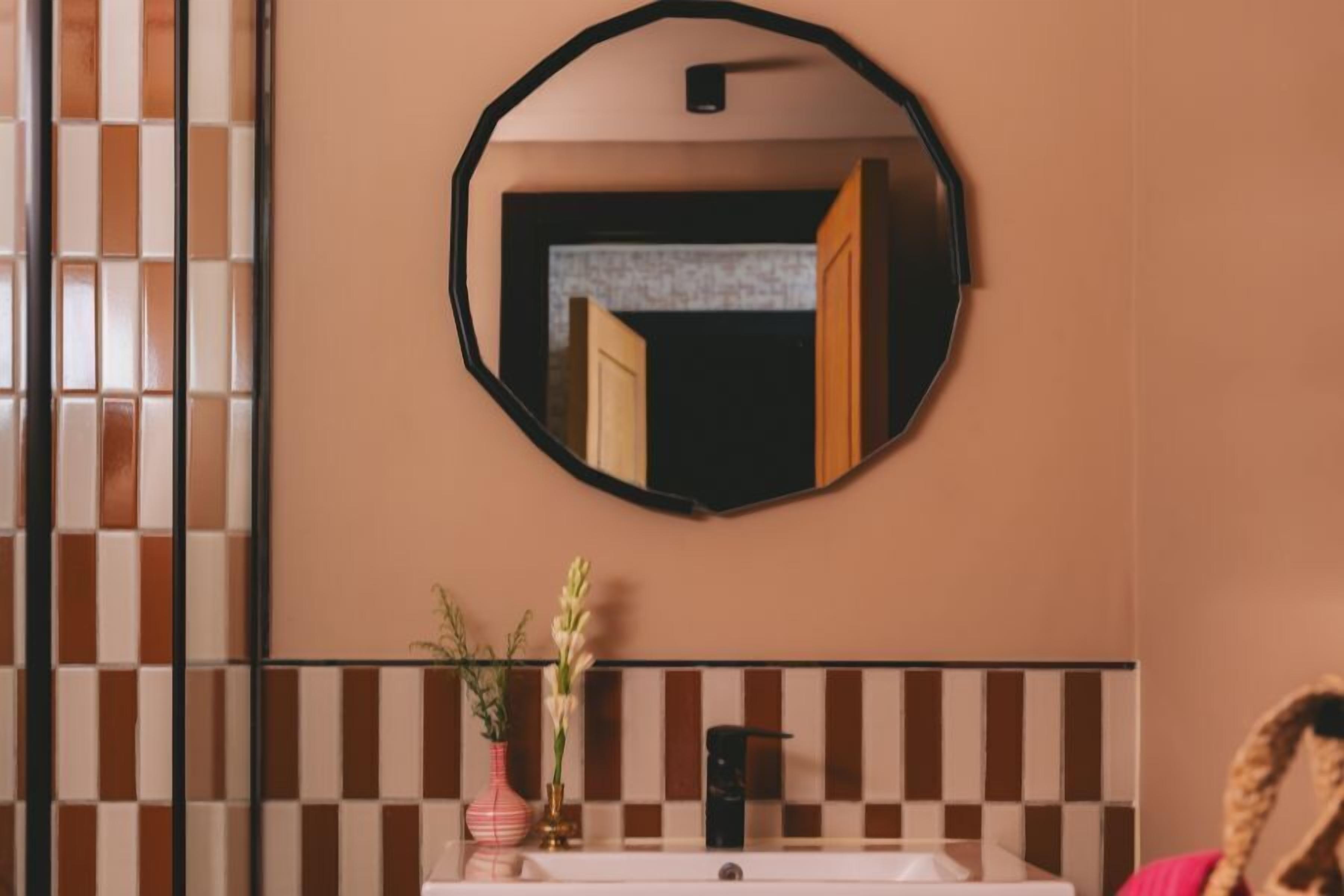 A bathroom with a round mirror, a white sink, and a tiled backsplash.