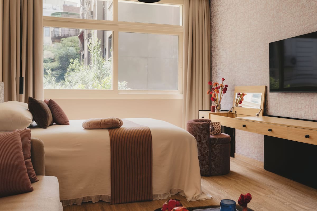 A bedroom with a bed, a dresser, a mirror, and a TV.