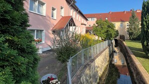 A pink building with a red roof, a narrow water channel, and a stone wall. - Ratskeller Hotel & Restaurant Lindow  (Lindow)