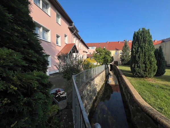 A narrow waterway flanked by buildings, a metal fence, and greenery. - Ratskeller Hotel & Restaurant Lindow  (Lindow)