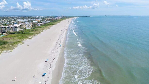 Ein Strand mit weitem Sandufer, einigen Sonnenschirmen und Gebäuden im Hintergrund.