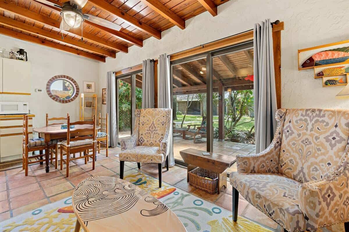 Amplia sala de estar con techo de madera, juego de comedor, sillas estampadas y un gran ventanal corredizo que da a un patio exterior.