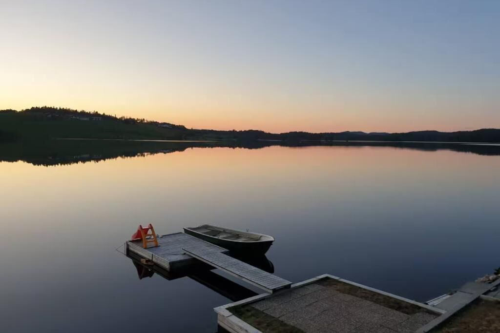 Un lago tranquilo con un muelle que se adentra en el agua, rodeado de un paisaje montañoso.