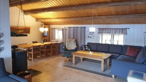Un salón acogedor con techo de madera, un sofá, una mesa de centro y una zona de comedor con una mesa y sillas.