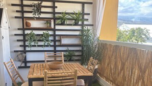 Un balcone con un tavolo e sedie di legno, circondato da piante in vaso e un muro decorativo.
