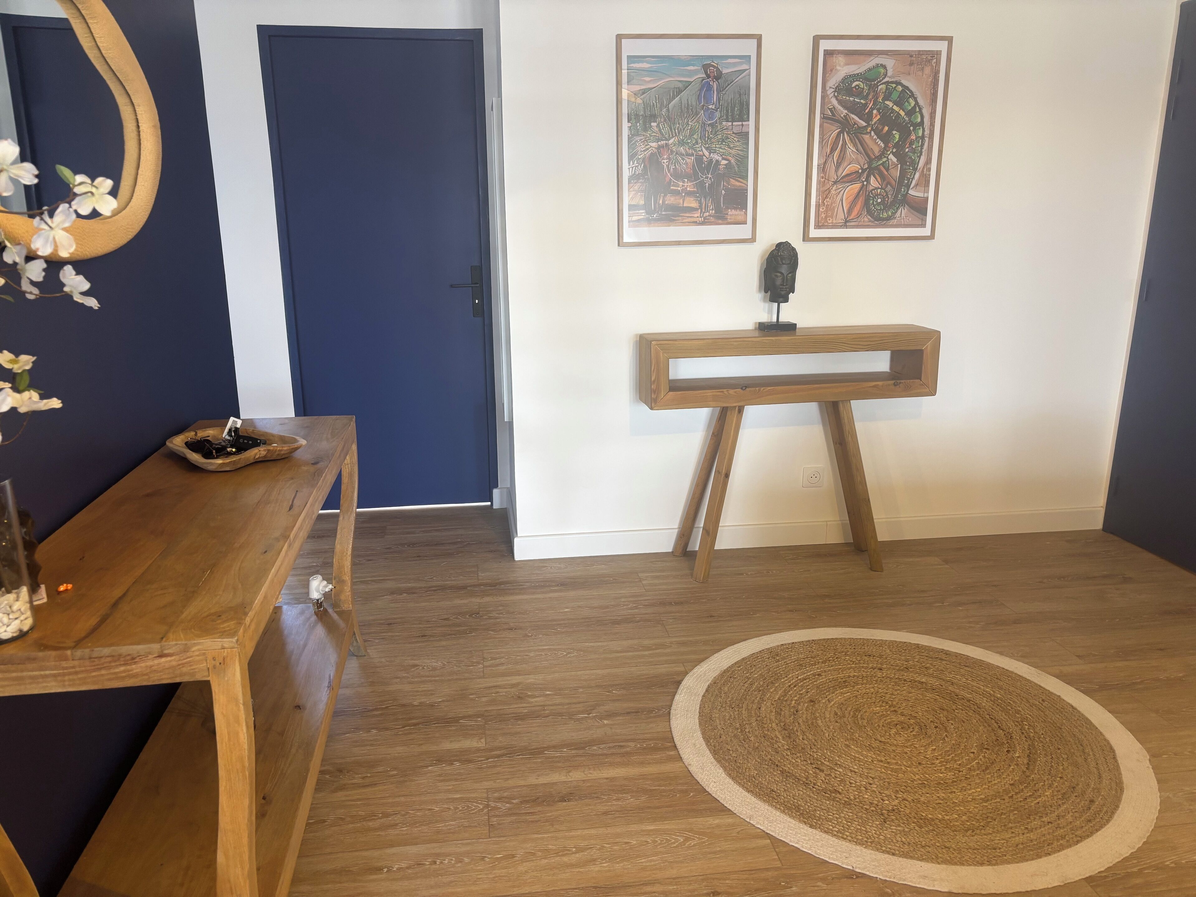Une pièce comprenant un banc en bois, un bureau debout, un tapis tissé et deux œuvres d’art encadrées accrochées au mur.