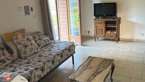 A cozy living room with a sofa, a coffee table, and a TV. There is a sliding glass door leading to an outdoor area. - Gîte near Honfleur (Gonneville-sur-Honfleur)