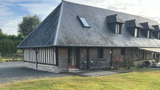 A two-story house with a sloped roof, a front porch with a bench, and a small garden area. - Gîte near Honfleur (Gonneville-sur-Honfleur)