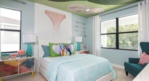 Une chambre à coucher comprenant un lit, une table de chevet, une chaise, une fenêtre et un mur agrémenté d’un objet décoratif.