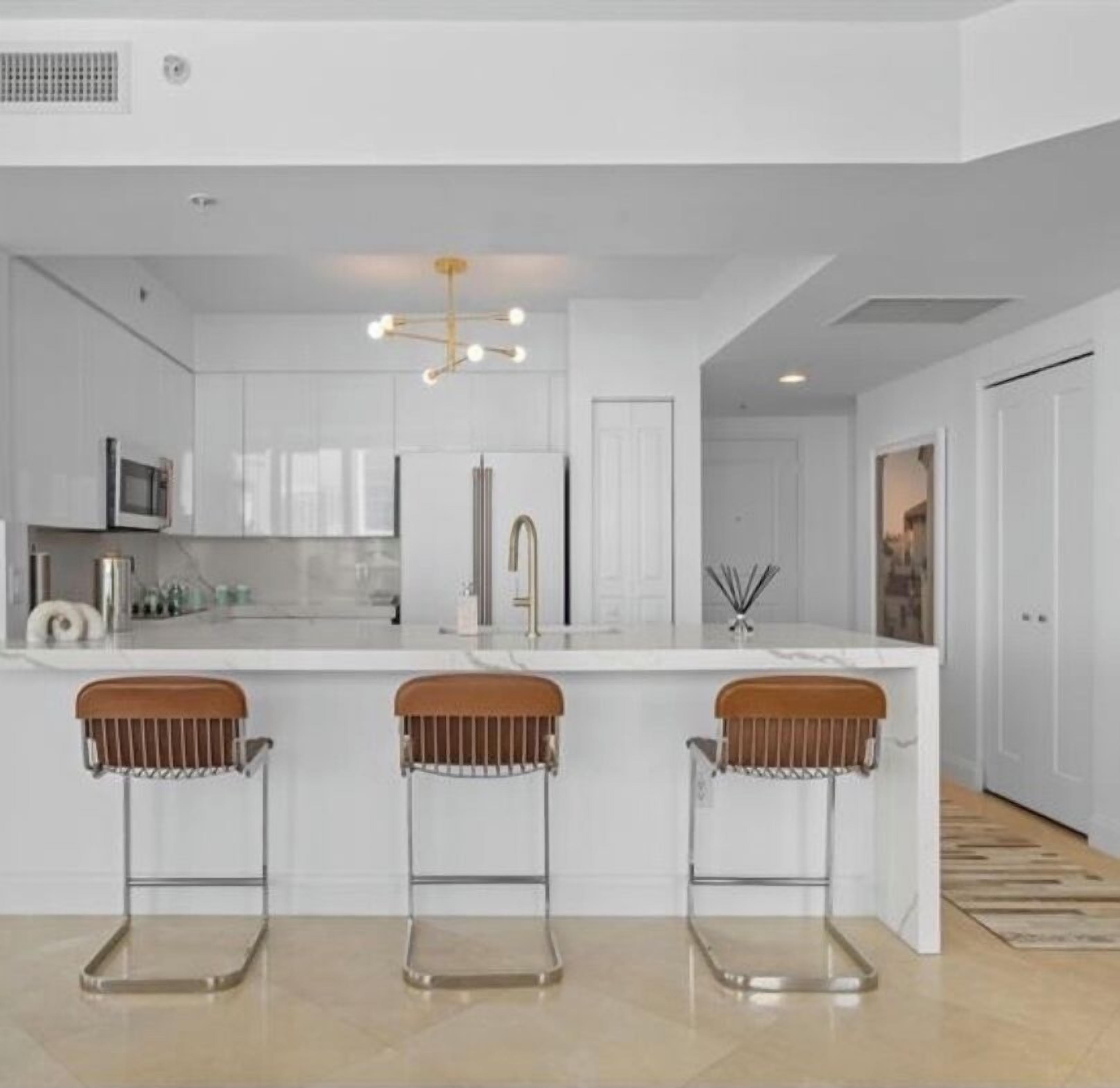A modern kitchen with white cabinetry, a central island with stools, a stainless steel refrigerator, and a pendant light.