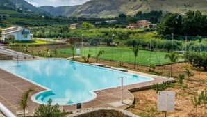 Una piscina de borde curvo, rodeada por una zona pavimentada y un campo de césped.