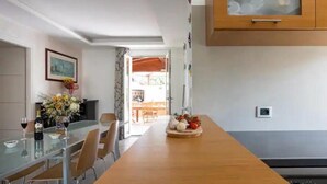 Un comedor con una mesa de vidrio, sillas, un jarrón con flores y un armario de madera encima.