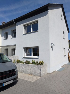 Ein modernes, zweistöckiges Gebäude mit weißer Fassade, zahlreichen Fenstern und einer gepflasterten Auffahrt.