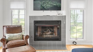 A living room with a fireplace, a leather armchair, and a television mounted above it.