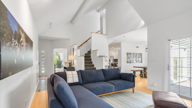 A modern living room with a blue sectional sofa, a wooden staircase, and a dining area.