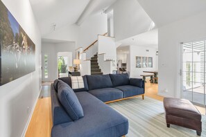A modern living room with a blue sectional sofa, a wooden staircase, and a dining area. - The Victory Lounge - 3B 3.5BA <1 mi to ND (South Bend)