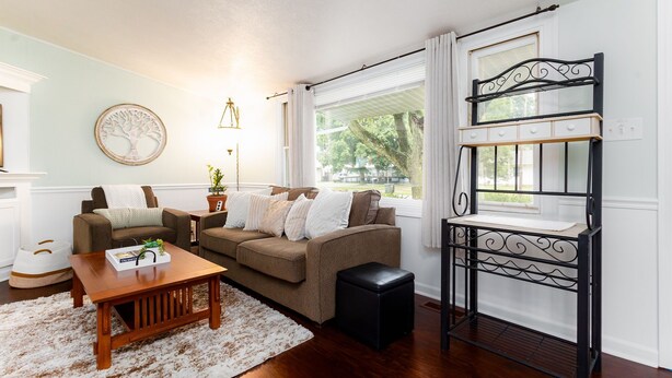 A living room with a brown sofa, a wooden coffee table, a black ottoman, and a decorative metal shelf.