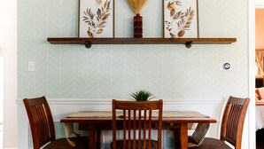 A dining area with a wooden table and chairs, a decorative shelf above, and a patterned wall.