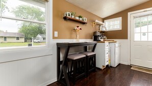 A kitchen with a wooden table and bar stools, a coffee machine, and a dish rack.