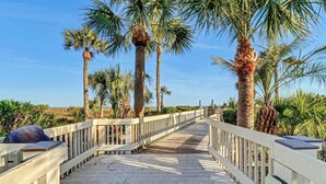 A wooden boardwalk with railings, surrounded by palm trees and vegetation. - Oceanfront Retreat 318 Breakers (Hilton Head Island)