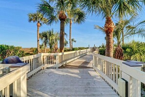 Une promenade en bois agrémentée de rampes blanches, bordée de palmiers et menant à une plage.