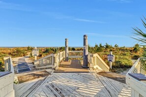 A wooden boardwalk leading to a beach with a fence and informational signs.