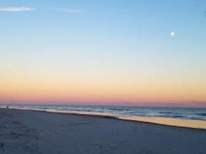 Une plage avec un ciel dégagé et une lune visible.