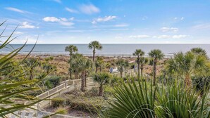 A coastal view with a wooden staircase leading down to a sandy area with palm trees and a clear blue sky. - Oceanfront Retreat 318 Breakers (Hilton Head Island)
