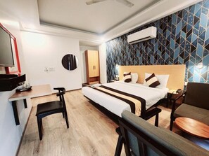 A hotel room with a bed, a desk, a chair, a sofa, and a TV. - Tipsyy inn 003 (Gurugram)