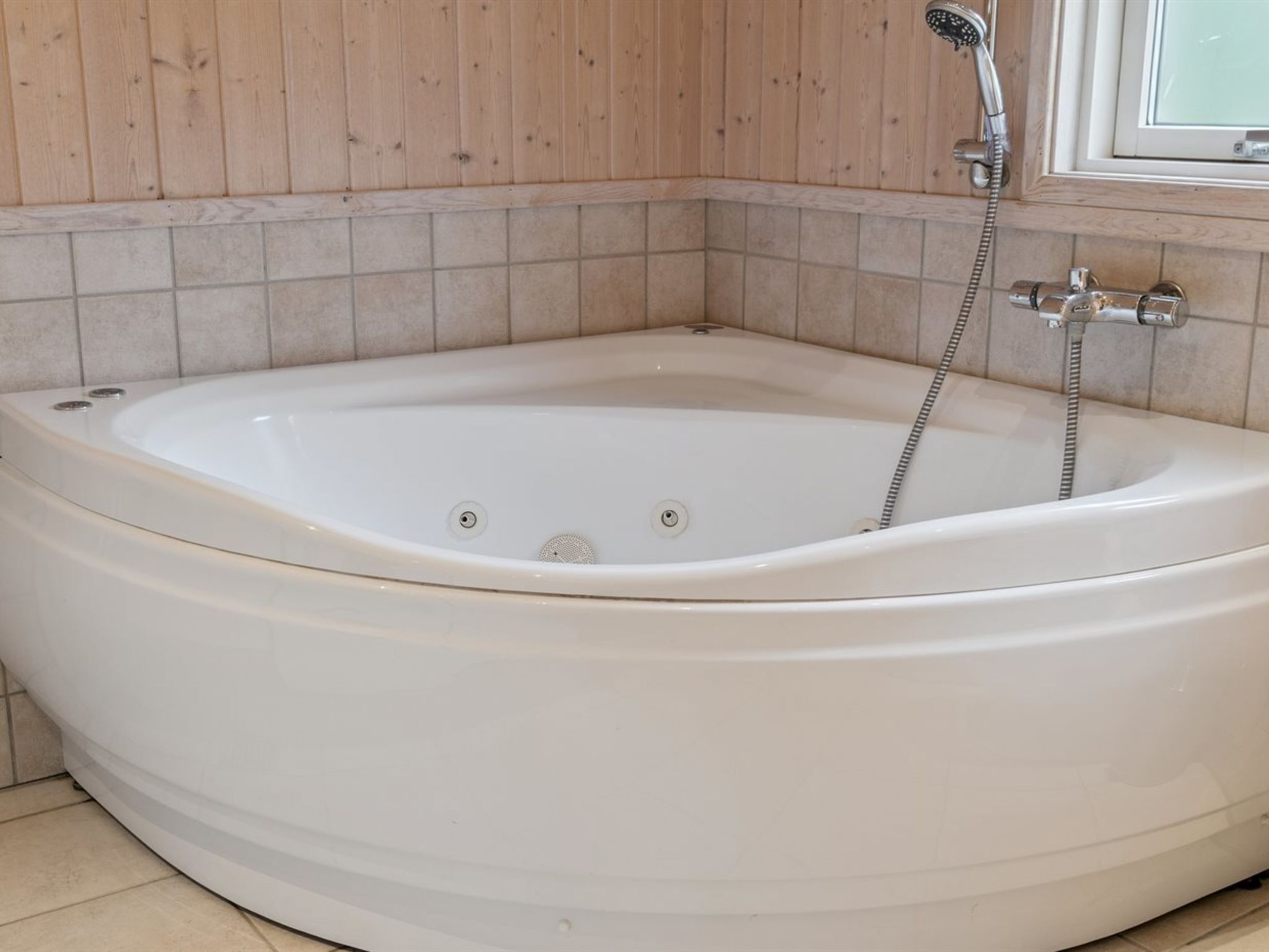 A corner bathtub with a showerhead and controls.